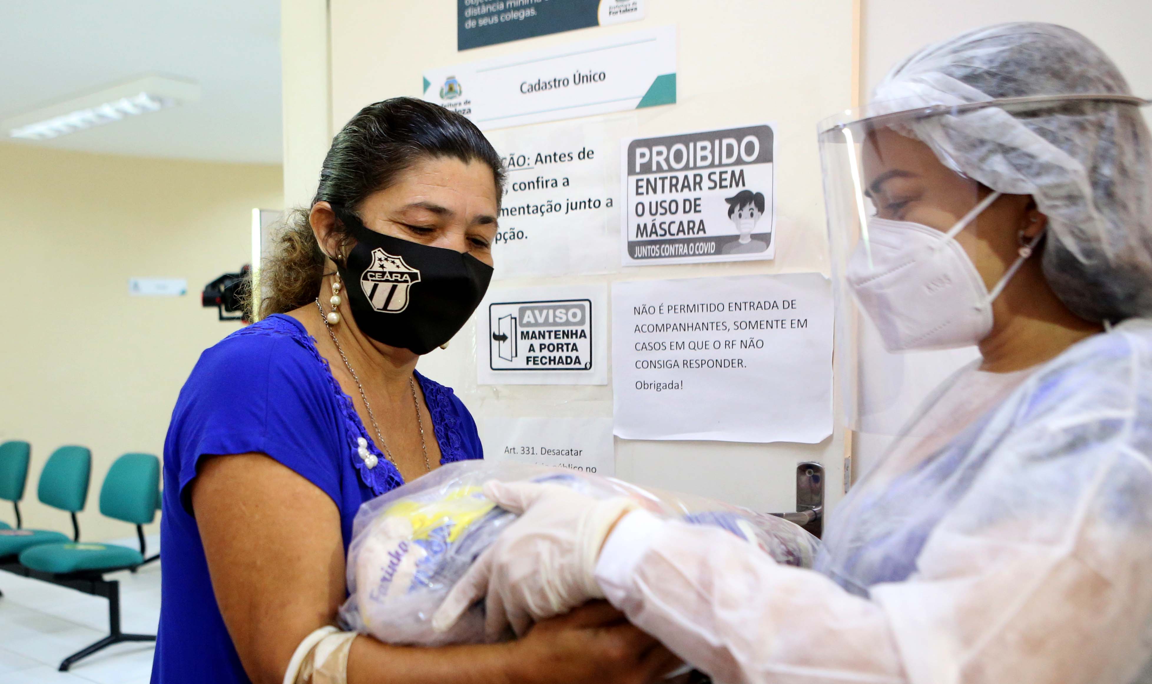 uma funcionária do CRAS entrega uma cesta básica para uma senhora